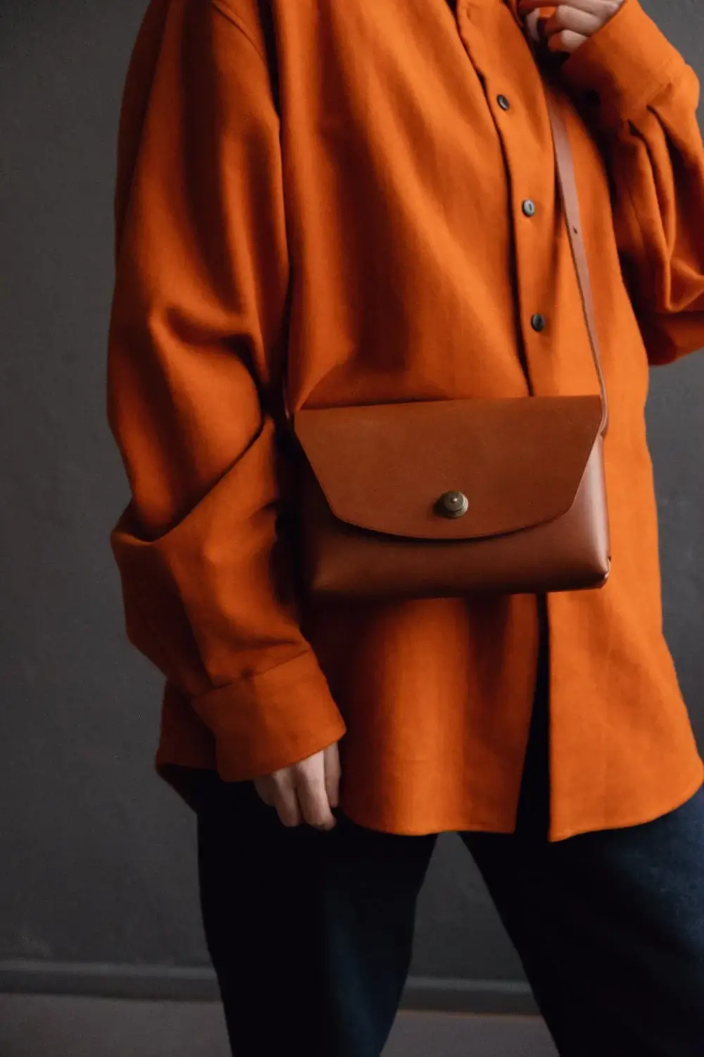 a woman in an orange shirt is holding a brown purse.