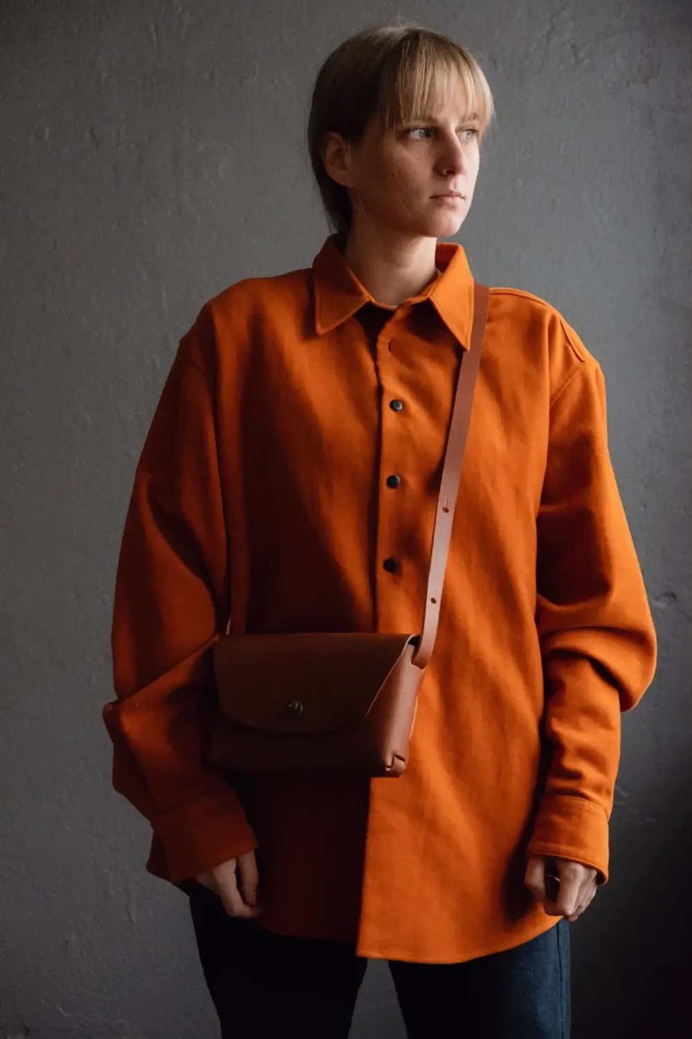 a woman in an orange shirt is holding a brown bag.