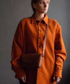 a woman in an orange shirt is holding a brown bag.