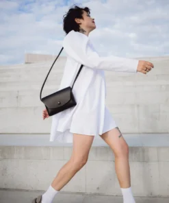 a woman in a white dress is carrying a black purse.