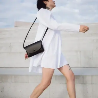 a woman in a white dress is carrying a black purse.