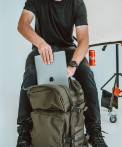 a man sitting on top of a backpack using a laptop computer.