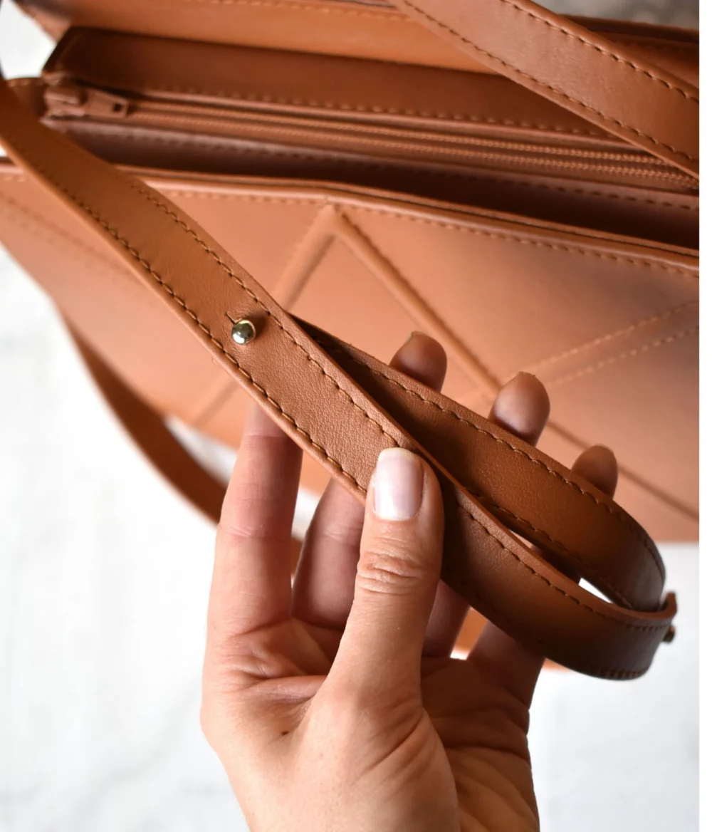 a hand holding a brown purse with a strap.