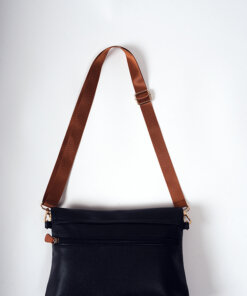 a black purse with a brown strap hanging on a wall.
