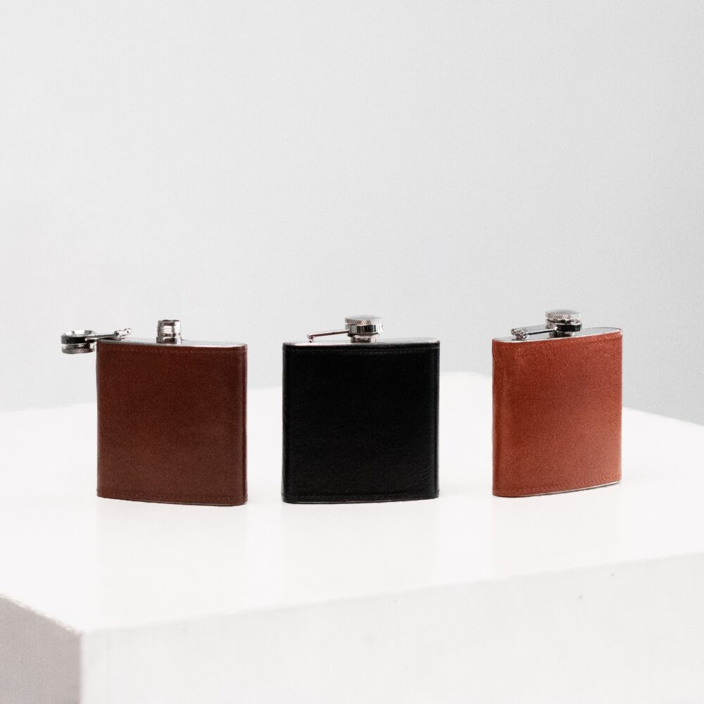 three leather flasks lined up on a white surface.