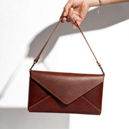 a woman's hand holding a brown envelope purse.