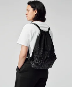a woman in a white t - shirt is wearing a black backpack.