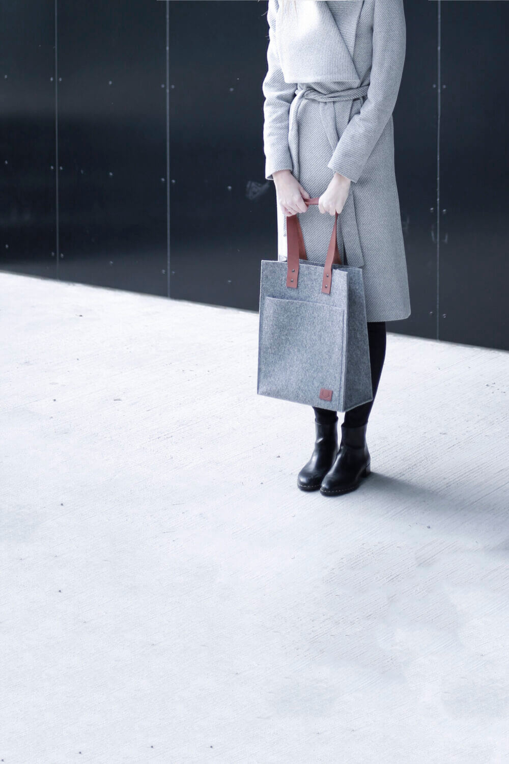 a woman in a gray coat holding a gray bag.