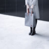 a woman in a gray coat holding a gray bag.