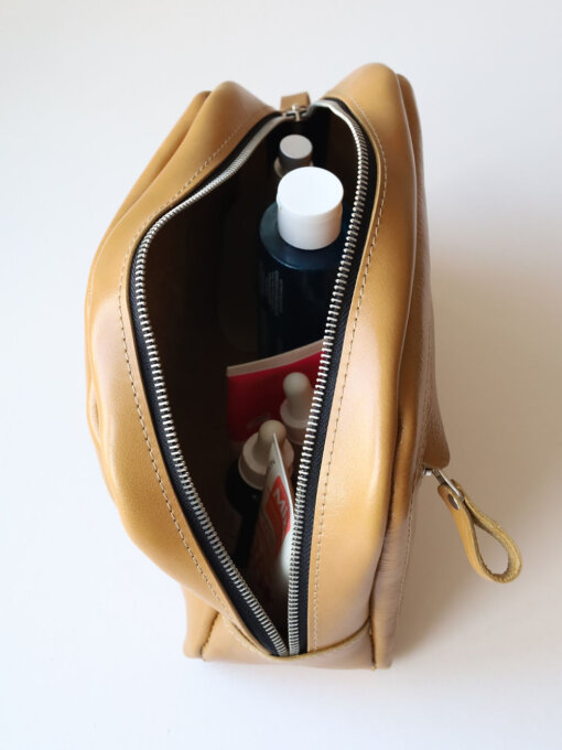 Un bolso de cuero color canela lleno de cosméticos y artículos de tocador.