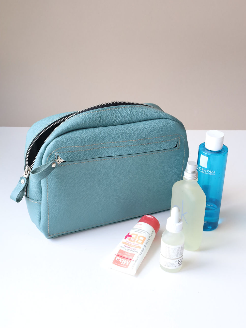 A DOUGLAS Toiletry Bag - Turquoise with cosmetics and a bottle of water.