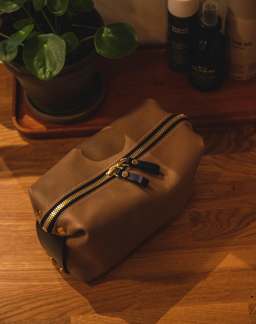 A tan leather Large Toiletry Bag Travel Mate on a wooden table.