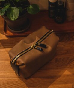 A tan leather Large Toiletry Bag Travel Mate on a wooden table.