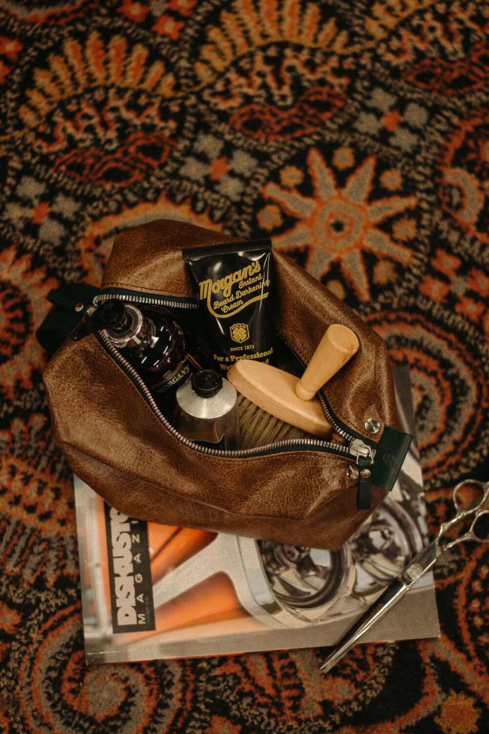 A brown leather Large Toiletry Bag Travel Mate with a pair of scissors on it.