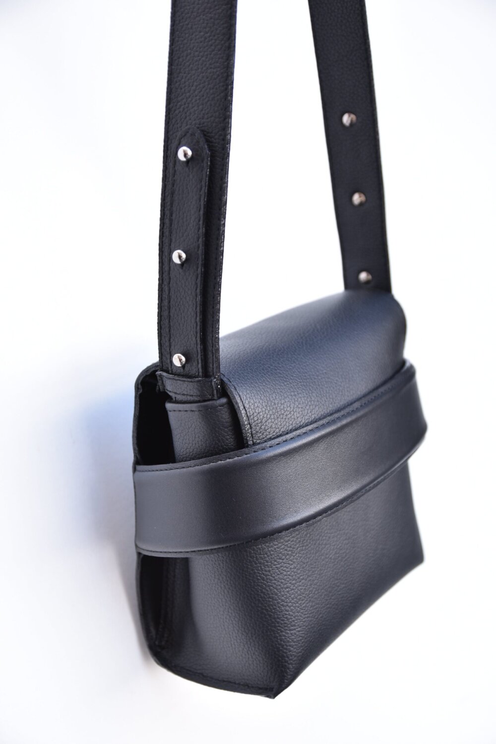 A black leather Shoulder bag Luce with straps hanging on a white background.