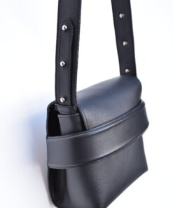 Un bolso de cuero negro con correas colgando sobre un fondo blanco.