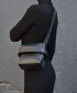 A woman wearing a black turtle neck dress and black leather Shoulder bag Luce - Black.