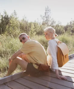 Una pareja joven sentada en un puente de madera con mochilas.