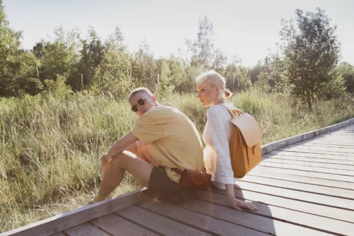 Una pareja joven sentada en un puente de madera con mochilas.