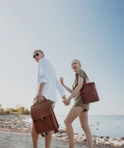 Hombre joven y mujer caminando por la playa con mochilas.