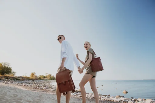 Hombre joven y mujer caminando por la playa con mochilas.